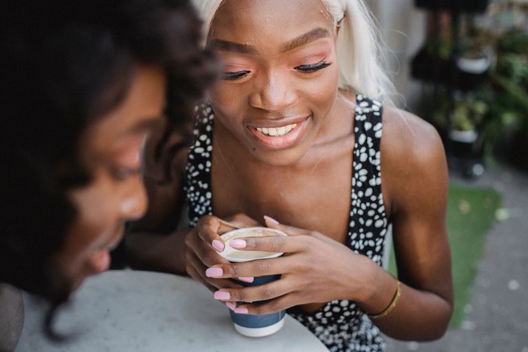 Two women sharing coffee and conversation outdoors, illustrating the value of relaxed social companionship.